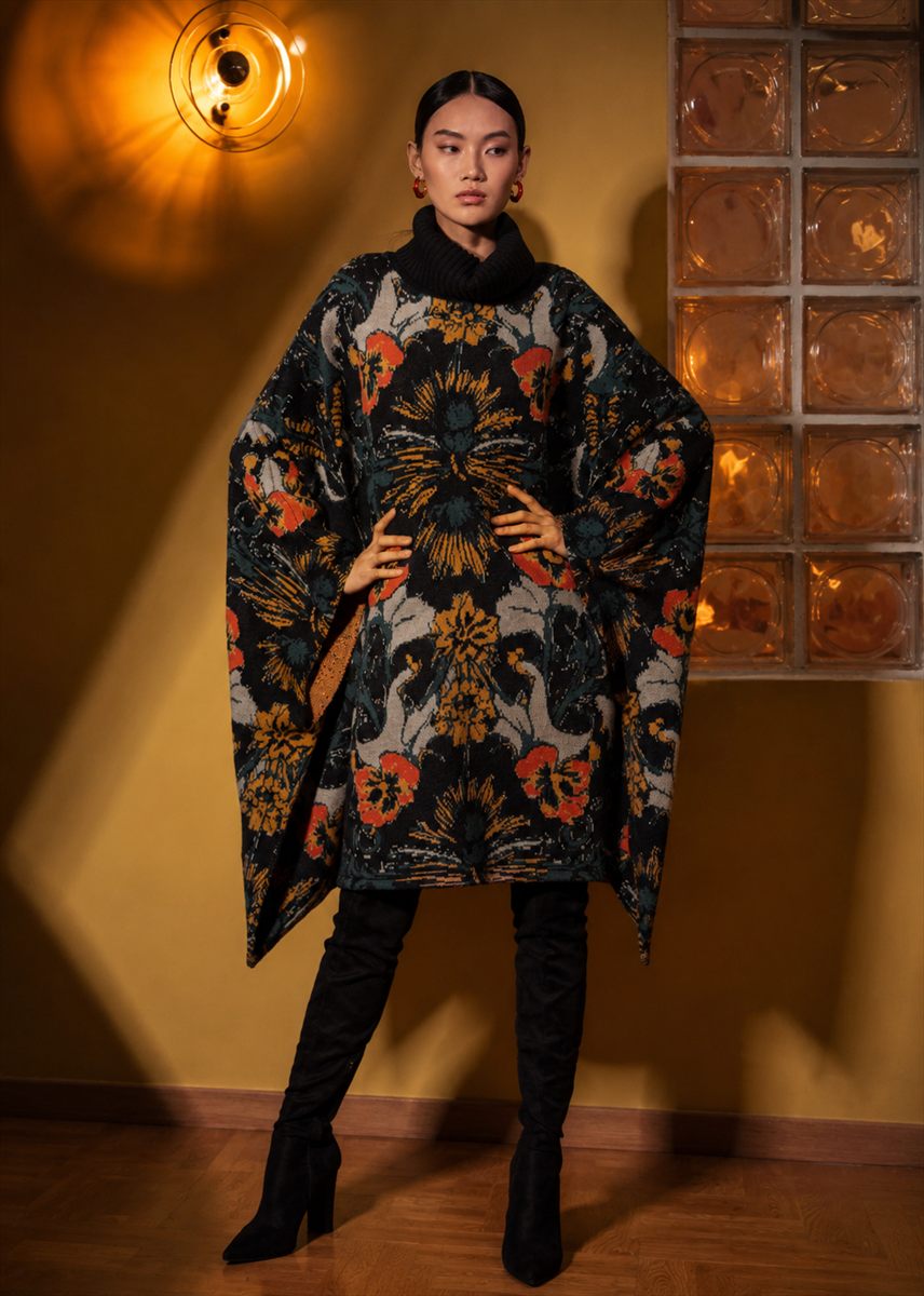 Model in a floral jacquard knit poncho with over-the-knee boots against an amber wall